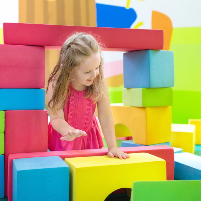 Child playing with colorful construction toy blocks. Educational toys for young kids. Kindergarten or preschool play room. Toddler kid at day care playground. Girl building house with block at daycare